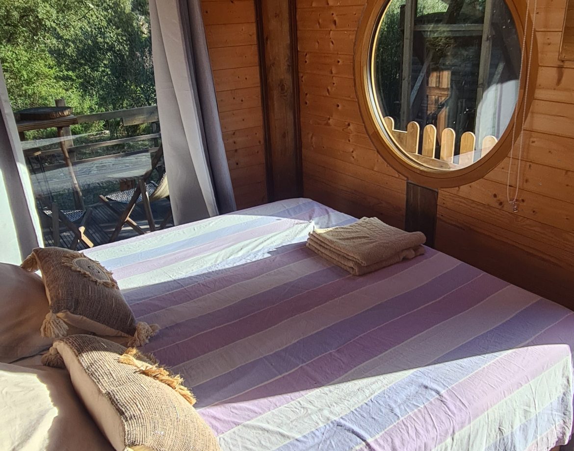 Chalet en bois à Corse, avec un lit confortable et une fenêtre ronde accueillante.