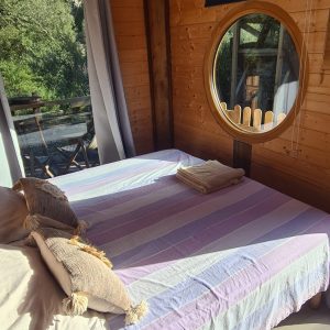 Chalet en bois à Corse, avec un lit confortable et une fenêtre ronde accueillante.