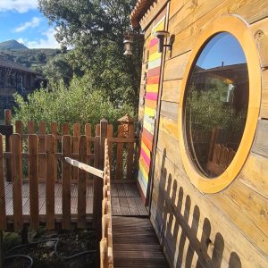 Cabane en bois colorée en Corse, avec une terrasse en bois et une vue verdoyante.