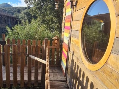 Cabane en bois colorée en Corse, avec une terrasse en bois et une vue verdoyante.