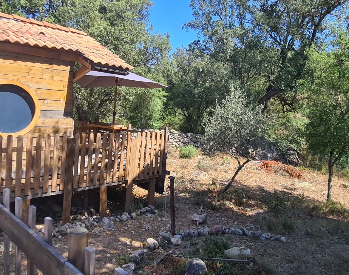 Cabane en bois colorée avec terrasse, entourée de verdure en Corse.