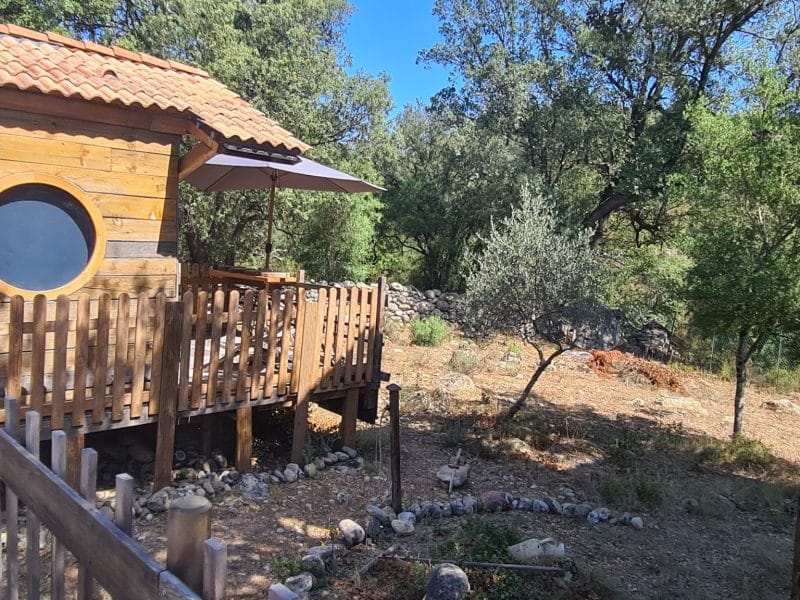 Cabane en bois colorée avec terrasse, entourée de verdure en Corse.