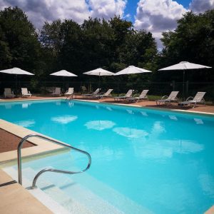 Hébergement insolite en Hauts-de-France avec piscine turquoise et chaises longues sous parasols.