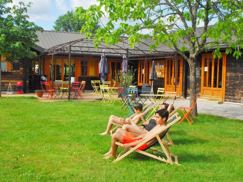 Chalet en bois avec chaises longues sur la pelouse, ambiance conviviale et ensoleillée.