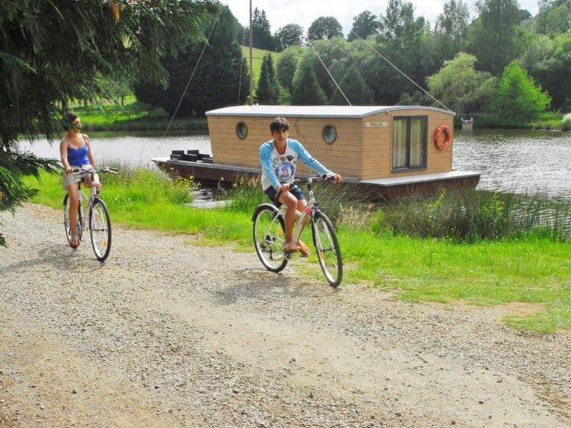 Cabane flottante au bord dun lac, avec des cyclistes sur un chemin de gravier.