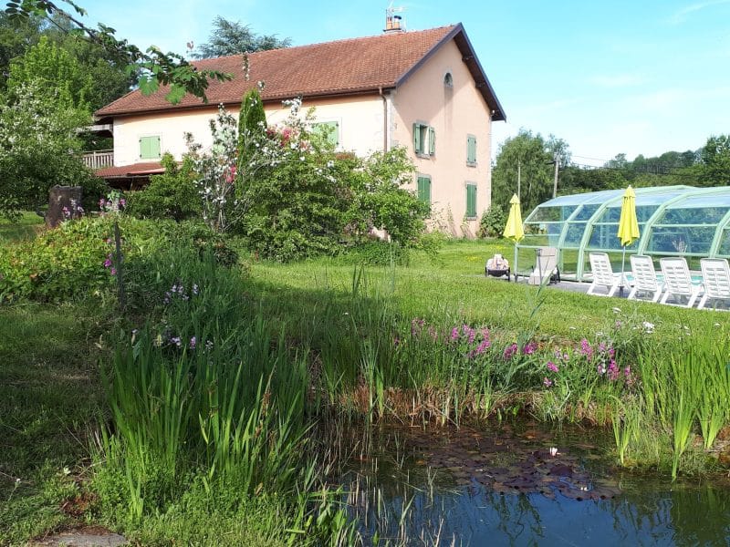 Maison dhôtes avec piscine couverte, entourée de verdure et de fleurs colorées.