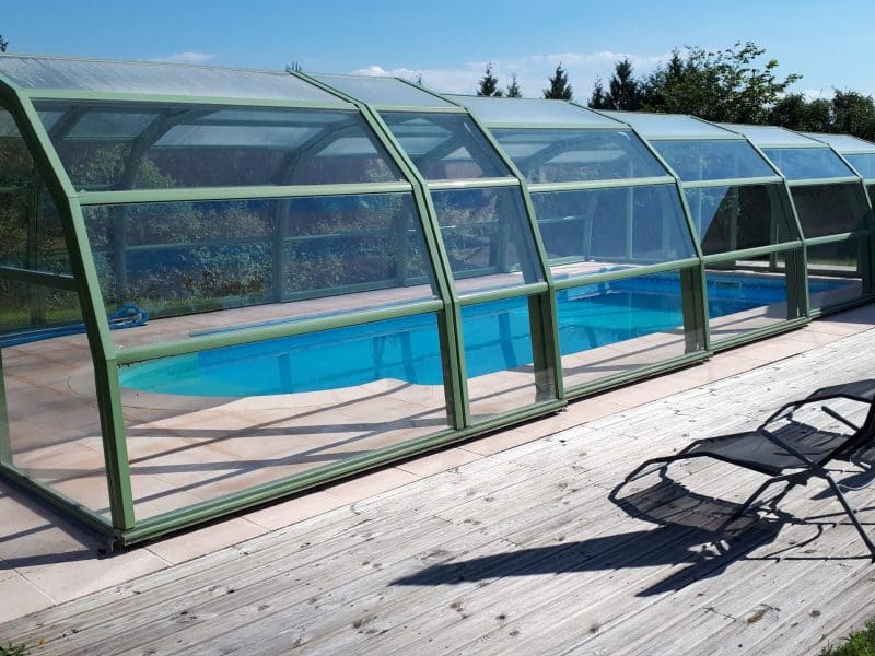 Gîte avec piscine couverte, entouré de verdure et chaises longues sur la terrasse.