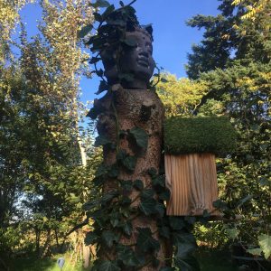 Cabane perchée dans un arbre, ornée de lierre et dune sculpture en bois.