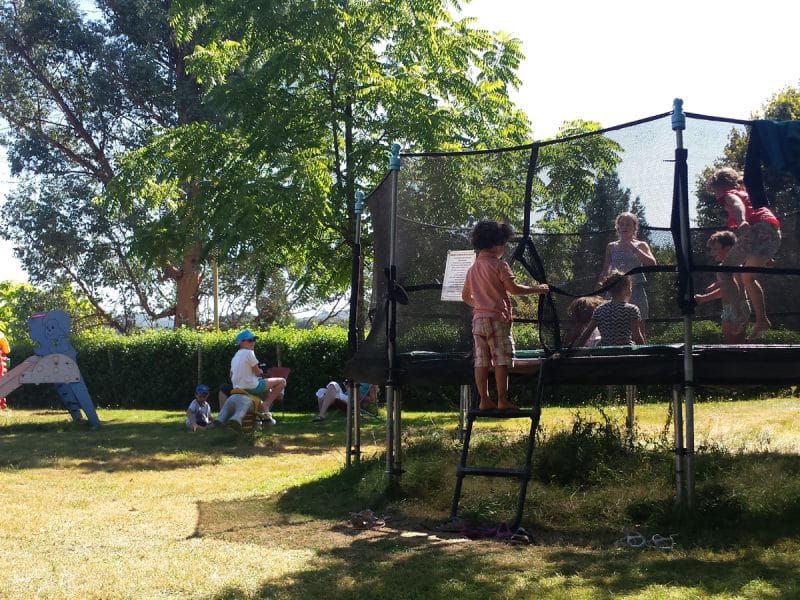 Hébergement touristique avec trampoline et aire de jeux pour enfants sous les arbres.