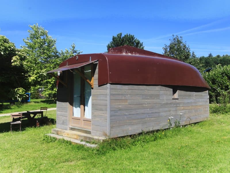 Cabane en bois avec toit arrondi, entourée de verdure et de nature apaisante.