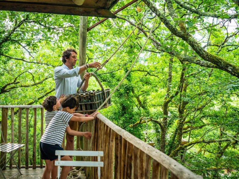 Cabane dans les arbres, vue sur la nature verdoyante, moment de partage en famille.