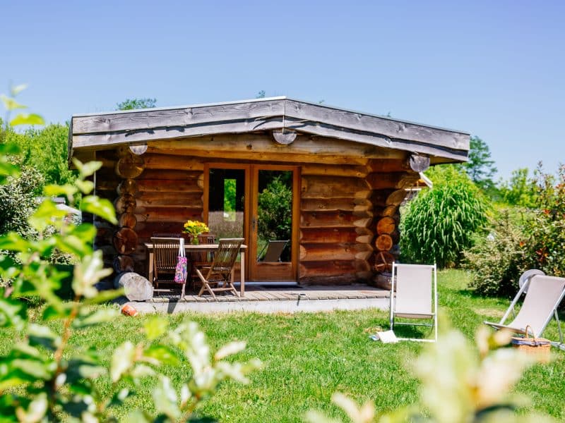 Chalet en bois avec terrasse, entouré de verdure et de chaises longues.