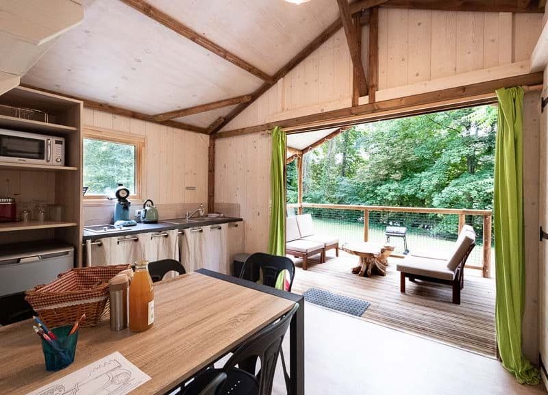 Chalet en bois lumineux avec cuisine ouverte et terrasse surplombant la forêt.