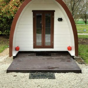 Hébergement insolite en forme de dôme, avec une entrée en bois et un jardin verdoyant.