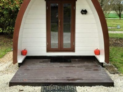 Hébergement insolite en forme de dôme, avec une entrée en bois et un jardin verdoyant.