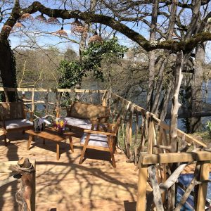 Cabane perchée en bois avec terrasse, vue sur la rivière et mobilier en bois.