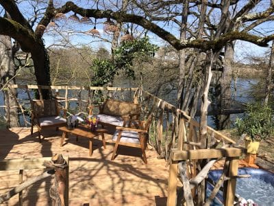Cabane perchée en bois avec terrasse, vue sur la rivière et mobilier en bois.