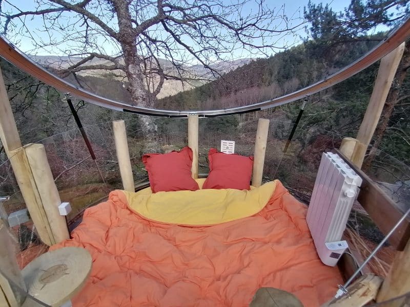 Cabane suspendue avec lit douillet, vue imprenable sur la nature environnante.