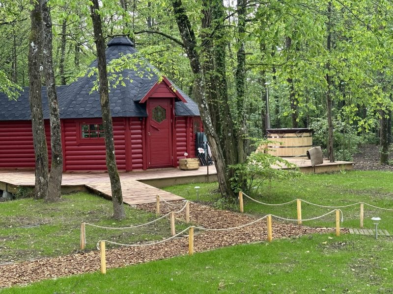 Cabane en bois rouge entourée darbres, avec un spa en bois à lextérieur.
