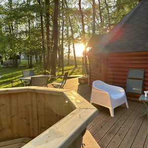 Cabane en bois avec terrasse, jacuzzi et lumière du soleil filtrant à travers les arbres.