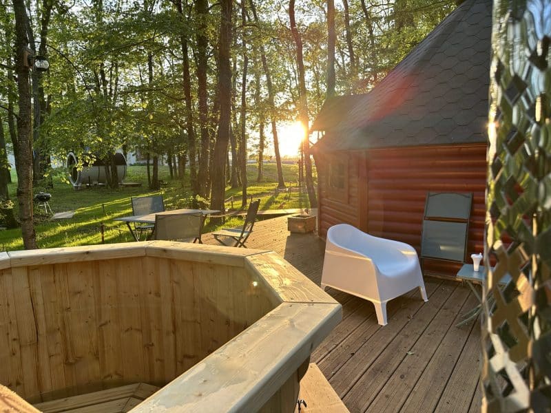 Cabane en bois avec terrasse, jacuzzi et coucher de soleil entre les arbres.