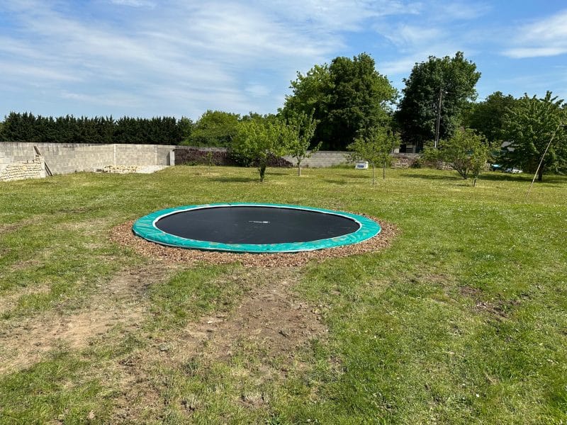Trampoline dans un jardin spacieux dun gîte rural, entouré darbres verdoyants.