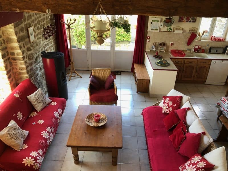 Gîte chaleureux avec canapés rouges et cuisine ouverte, ambiance conviviale.
