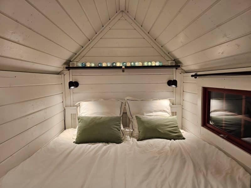 Chalet cosy avec lit double, murs en bois blanc et éclairage doux.