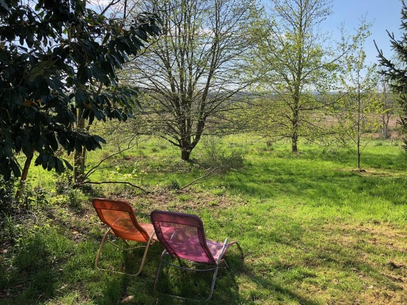 Chalet en pleine nature avec chaises colorées face à un paysage verdoyant.