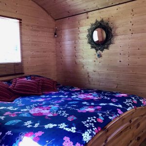 Chalet en bois à Basse-Normandie, intérieur chaleureux avec lit douillet et décor floral.