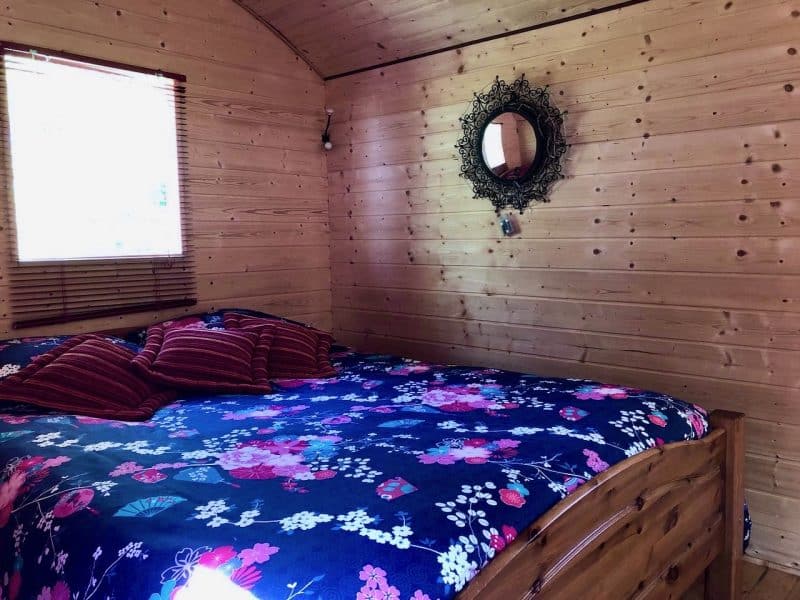 Chalet en bois avec lit douillet, décoré de coussins colorés et dun miroir élégant.