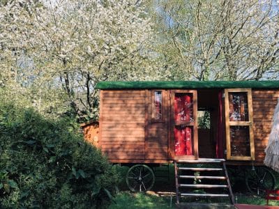 Roulotte en bois nichée sous des arbres fleuris en Basse-Normandie.