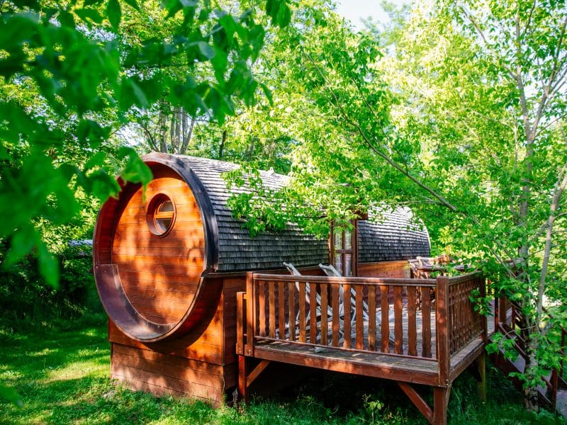 Cabane en bois en forme de tonneau, entourée de verdure luxuriante.
