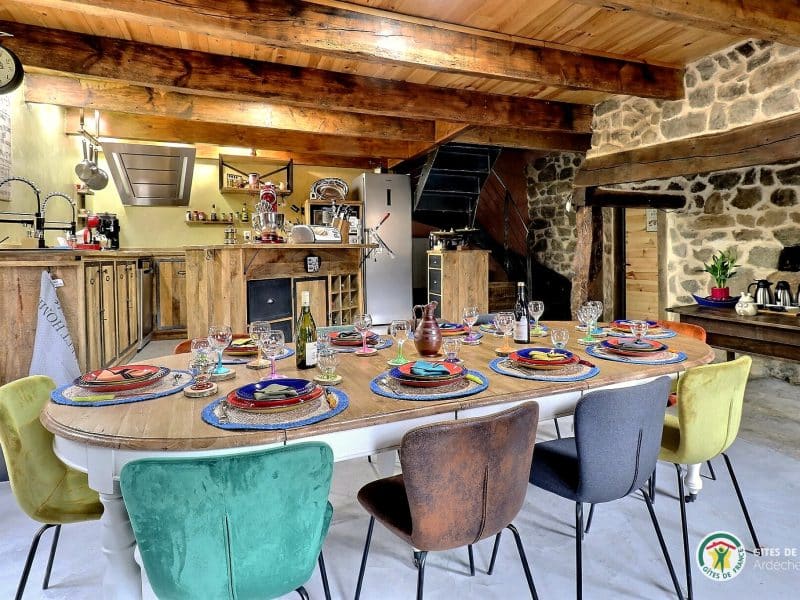 Gîte chaleureux avec une grande table à manger colorée et une cuisine en bois.
