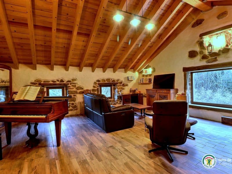 Gîte chaleureux avec poutres en bois, piano et vue sur la nature.