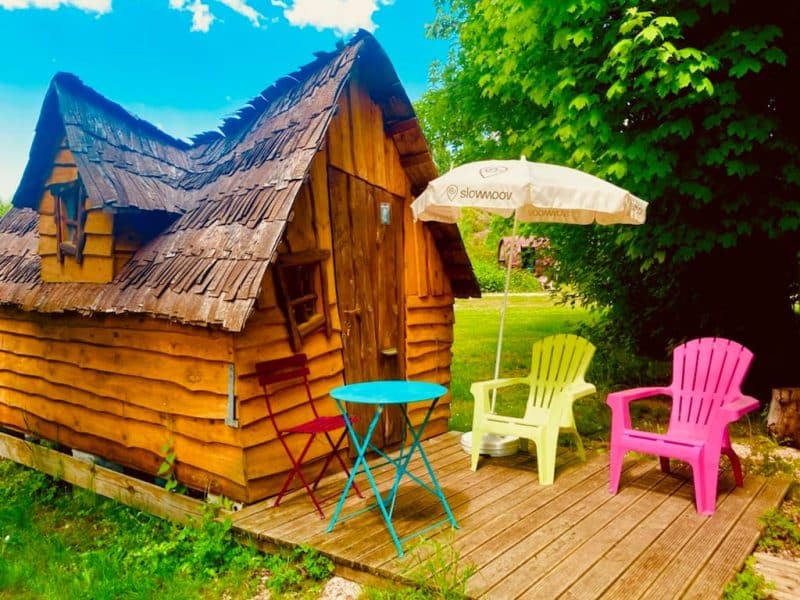 Charmante cabane en bois avec terrasse et chaises colorées sous un parasol.