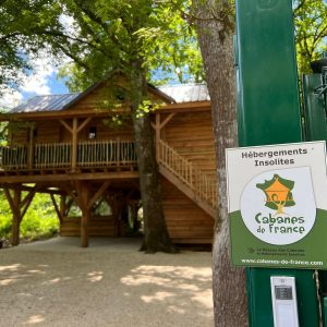 Cabane en bois perchée, entourée darbres, offrant un séjour insolite au cœur de la nature.