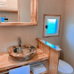 Salle de bain dun hébergement insolite en bois, avec un lavabo en bois sculpté.