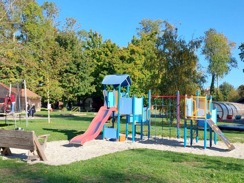 Aire de jeux colorée dans un camping, entourée darbres verdoyants.
