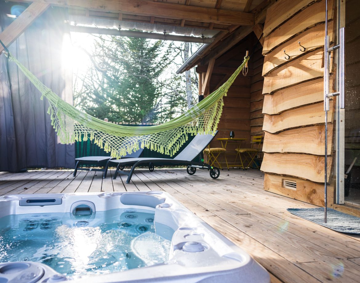 Cabane en bois avec jacuzzi et hamac, ambiance chaleureuse et détente assurée.