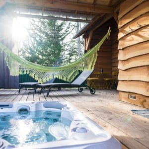 Cabane en bois avec jacuzzi et hamac, ambiance chaleureuse et détente assurée.