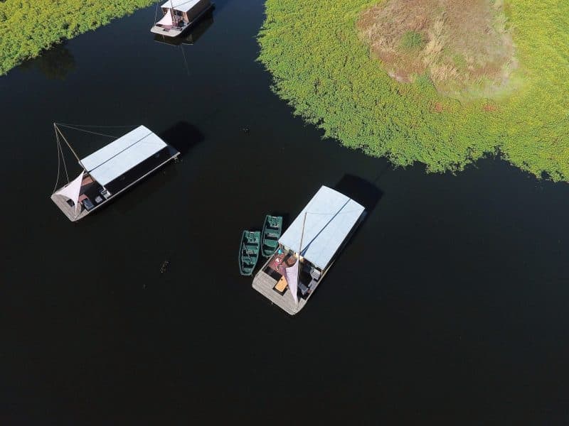 Hébergement flottant sur un lac, avec des bateaux amarrés et une végétation luxuriante.