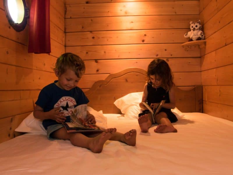 Chalet en bois chaleureux avec enfants lisant sur un lit douillet.