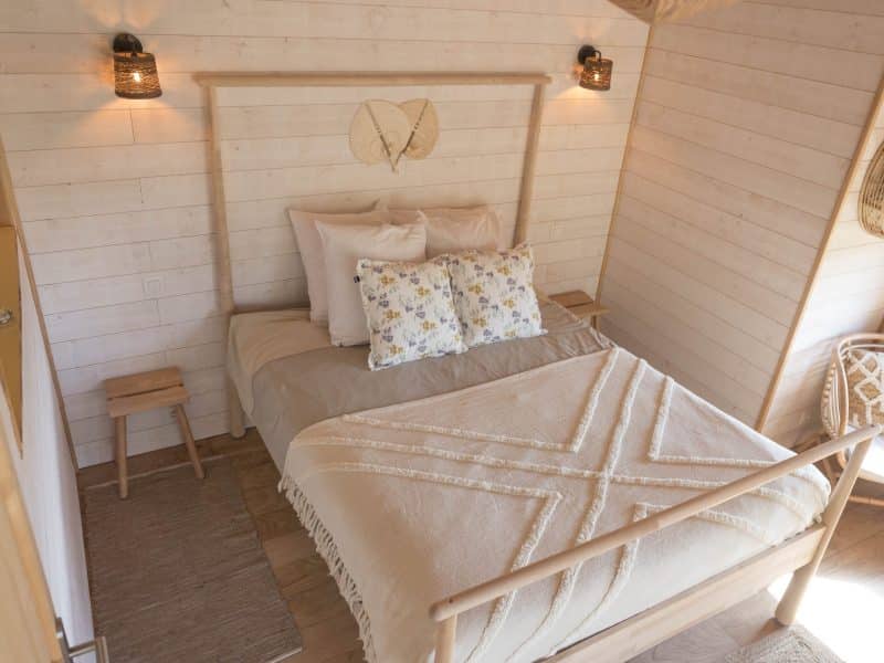Chalet cosy avec lit douillet, décoré de coussins fleuris et lumière chaleureuse.