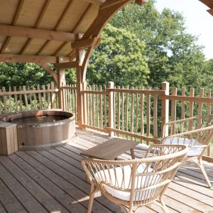 Cabane en bois en Bretagne avec terrasse, jacuzzi et chaises confortables.