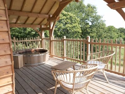 Cabane en bois en Bretagne avec terrasse, jacuzzi et chaises confortables.