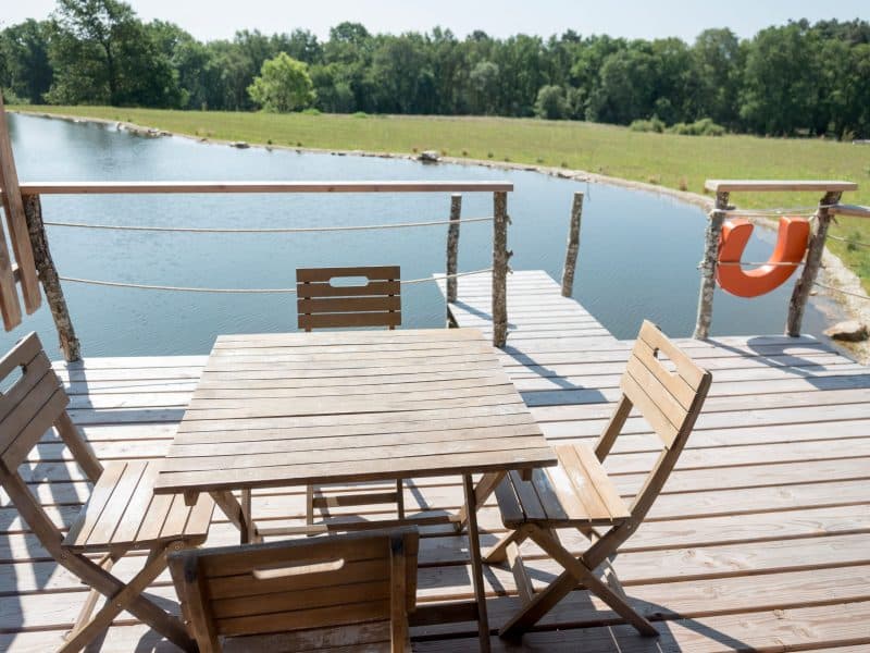 Terrasse en bois dun chalet au bord dun étang, avec vue sur la nature.