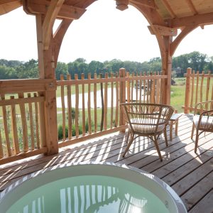 Cabane en bois avec jacuzzi, terrasse ensoleillée et vue sur la nature bretonne.