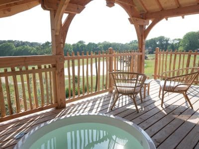 Cabane en bois avec jacuzzi, terrasse ensoleillée et vue sur la nature bretonne.
