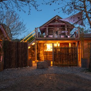 Cabane en bois illuminée, entourée darbres, offrant un cadre unique en Midi-Pyrénées.